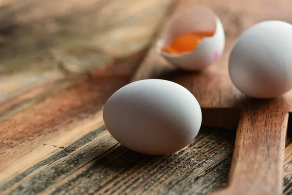 Chicken eggs and half broken egg with yolk on wooden backgroun