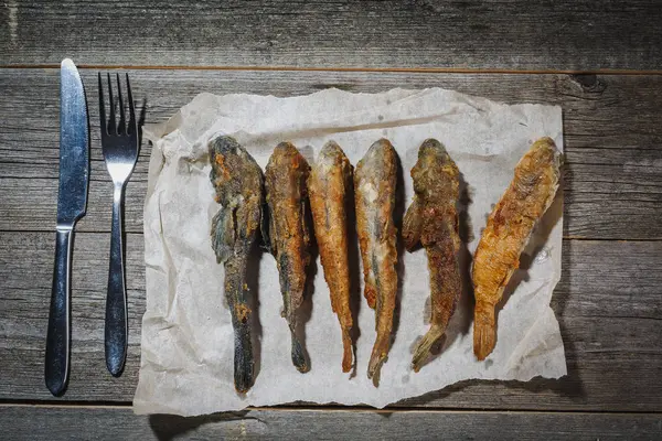 Pescado seco con tenedor y cuchillo en la mesa. Pescado de río seco salado sobre un fondo impresionante de madera. Pescado seco al sol. Peces de mar . — Foto de Stock