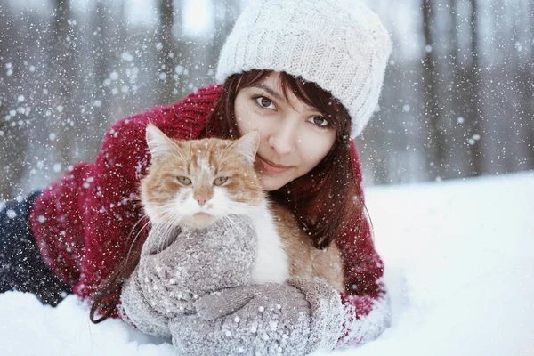 Menina bonita com em suéter vermelho e chapéu segurando e brincando com pouco gato fofo no inverno parque nevado. Animais de estimação, conforto, Natal, inverno e as pessoas conceito jovem mulher com gato em pé ao ar livre . — Fotografia de Stock