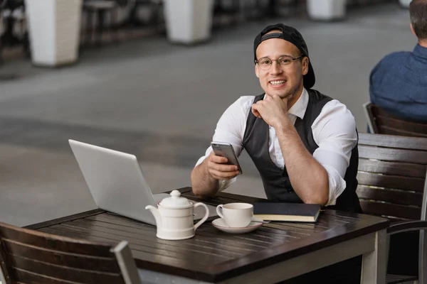 Hombre de negocios que trabaja con el ordenador portátil y el teléfono en la cafetería al aire libre — Foto de Stock
