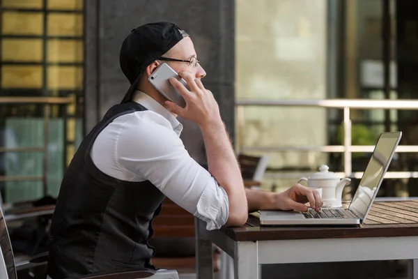 Joven hombre de negocios que trabaja con el ordenador portátil y teléfono en la cafetería al aire libre — Foto de Stock