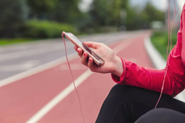 Primer plano sentada corredor femenino sosteniendo el teléfono celular y escuchando música —  Fotos de Stock