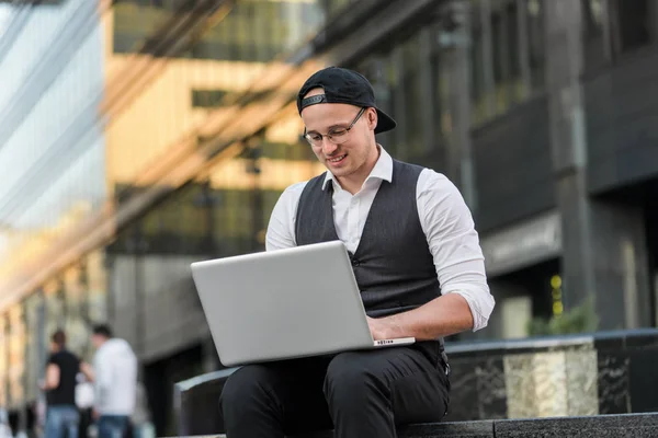 Handsome young student working with laptop outdoors.