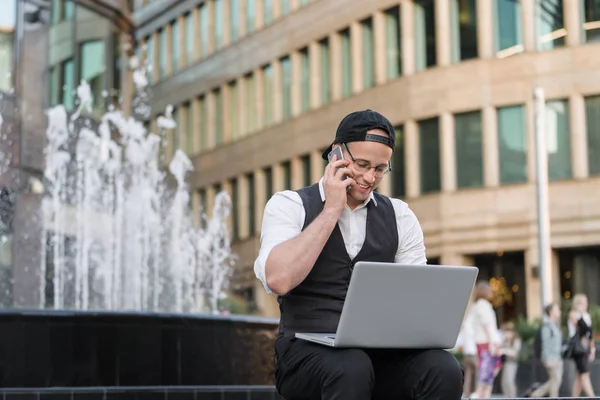 Joven hombre de negocios trabajando con el ordenador portátil y teléfono al aire libre Imagen de archivo