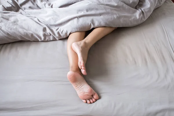 赤脚和腿下毯子在床上 — 图库照片