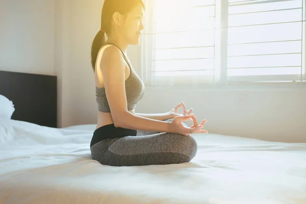 年轻的亚洲妇女坐在床上练习做瑜伽练习 在家醒来后锻炼 健康和生活方式的概念 选择性的焦点 — 图库照片