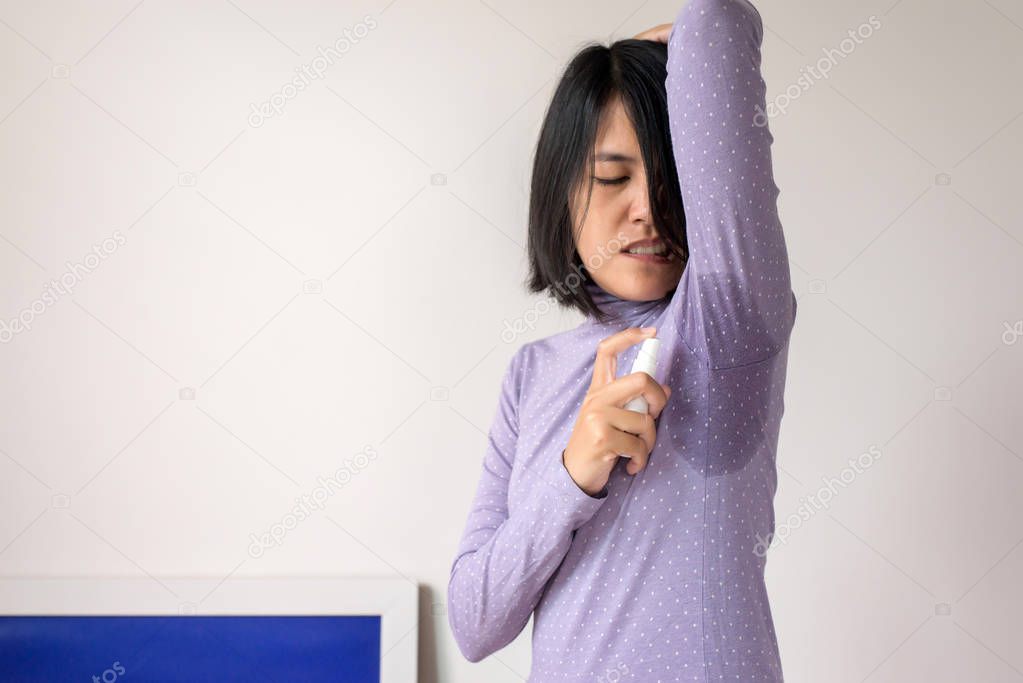Asian woman using spray with odor sweating,Female smelling or sniffing her armpit,Bad smell,Copy space for text and white background