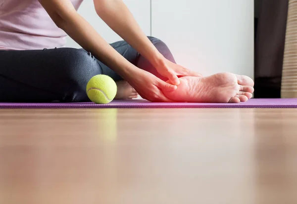 Woman hands massage to her foot on yoga mat at home,Feet soles massage for plantar fasciitis,Close up
