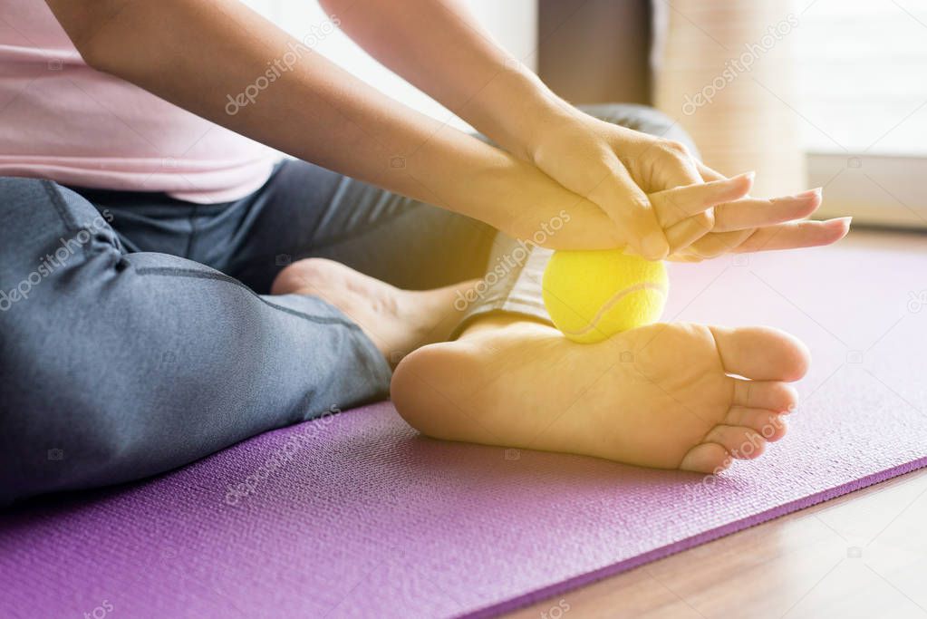 Woman hands using tennis ball to her foot on yoga mat,Feet soles massage for plantar fasciitis,Close up