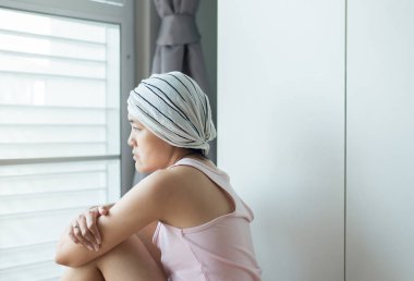 Kanser hastası Asyalı bir kadın bir şeye bakıyor ve evinde oturuyor. Kadın depresyonda ve üzgün.