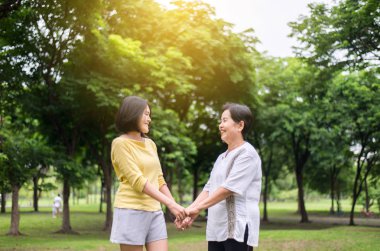 Kendine iyi bak ve destek ol, kızı ile birlikte parkta el ele tutuşan, mutlu, gülümseyen, pozitif düşünen yaşlı Asyalı kadının portresi.