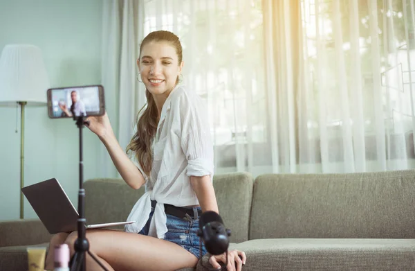 Beautiful woman blogger showing and demonstration cosmetic product on mobile phone camera screen at home