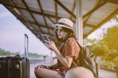 Güzel Asyalı kadın turist akıllı telefon kullanıyor ve tren istasyonunda bekliyor, seyahat ve tatil konsepti.