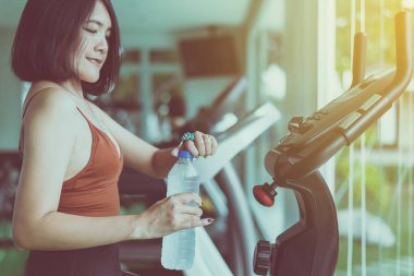 Çekici bir kadın spor salonunda oturup su içiyor, Asyalı bir kadın spor yaptıktan sonra dinleniyor.