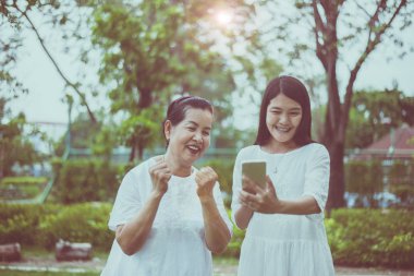 Neşeli Asyalı anne-kız selfie 'si cep telefonuyla birlikte doğada, kız dikkat ve destek, yaşlı sosyal asya konsepti