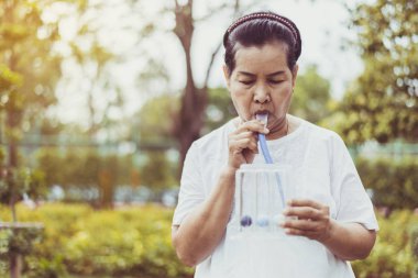 Yaşlı Asyalı anne doğada akciğeri uyarmak için spirometre ya da üç top kullanıyor.