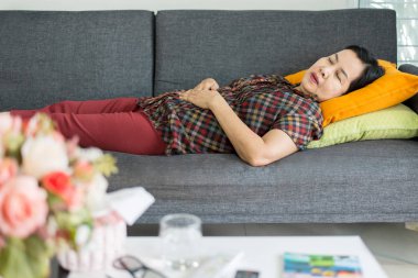 Karın ağrısından muzdarip son sınıf öğrencisi yaşlı bir Asyalı kadın karın ağrısı çekiyor ve kanepede yatıyor.