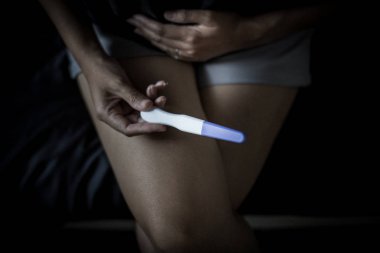 Yatak odasında hamilelik testi yaptıktan sonra kadının eli karnına dokunuyor.