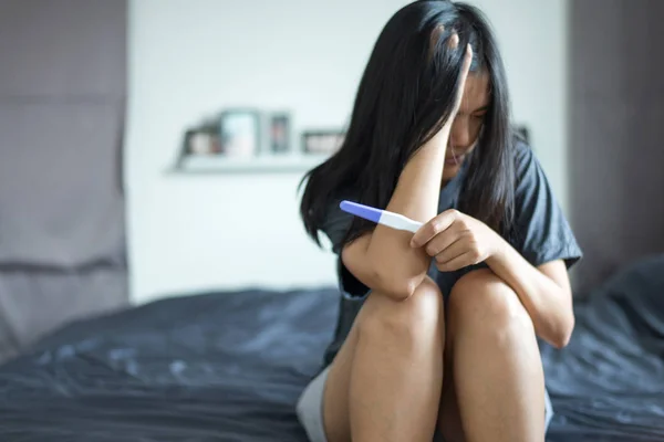 Hamilelik testinden sonra Asyalı depresyondaki kadın yatak odasında oturuyor.