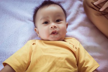 Sevimli Asyalı erkek bebek yatağa uzanıyor, anne özen ve destek veriyor, çocukluk ve bebek bakımı kavramı.