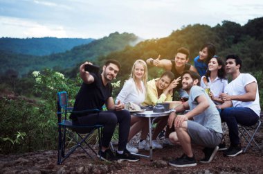 Doğada cep telefonları olan, mutlu ve gülümseyen, sırt çantasından keyif alan çok ırklı gezgin selfie grubu.
