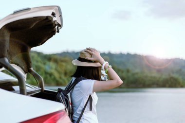 Hipster genç Asyalı kadın gezgin dışarıda arabada cep telefonuyla oturmuş, dinleniyor, pozitif düşünüyor.