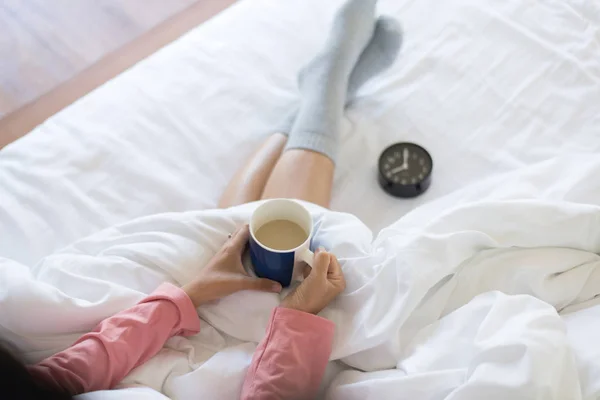 女人的手拿着一杯热咖啡 坐在床上的毛毯下 放松一下时间 — 图库照片