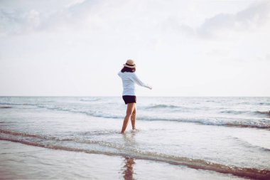 Gün batımında sahilde yürüyen mutlu genç bir kadın, dinlenme zamanı, olumlu düşünme.