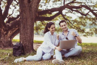 Genç çiftler parkta dizüstü bilgisayar kullanıyorlar. Romantik ve mutlu anların tadını çıkarıyorlar.