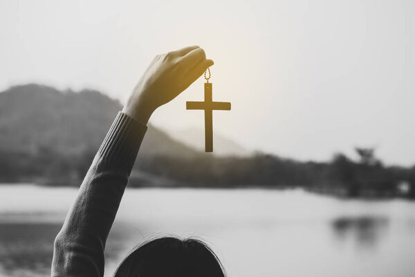 Женщина держит крест распятия Иисуса Христа на природе, черно-белая тонировка
