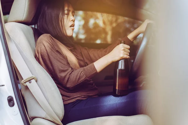 Drunk asian woman drinking alcohol while driving car on road,Women drives her car with a bottle of beer,Dangerous driving concept