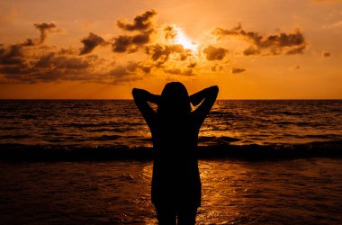 Mutlu kadın silueti ellerinin başının üstünde dururken günbatımı denizde, Özgürlük konsepti