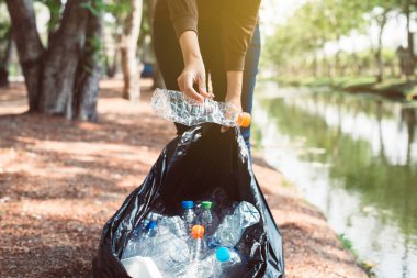Kamu parkında plastik şişe taşıyan siyah renkli çöp torbası tutan gönüllü kadın, geri dönüşüm ve atık yönetimi kavramını yok et