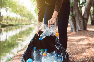 Kamu parkında plastik şişe taşıyan siyah renkli çöp torbası tutan gönüllü kadın, geri dönüşüm ve atık yönetimi kavramını yok et, iyi bilinçli zihin.