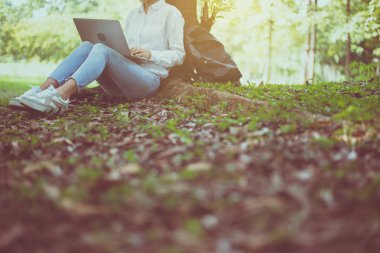 Sabahları parktaki dizüstü bilgisayarını kullanan mutlu ve gülümseyen genç bir bayan.