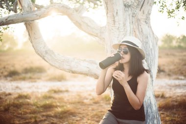 Ormanda günbatımında şişeden su içen mutlu Asyalı kadın, yaşam tarzı açık hava yolculuğu konsepti.