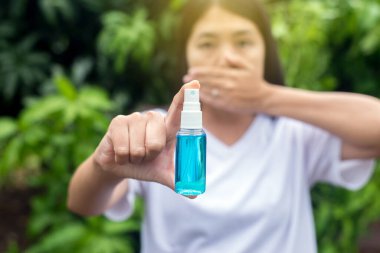 Asyalı kadın elleri sprey şişesinde dezenfektan jeli gösteriyor. Doğa, hijyen koronavirüsü koruması.