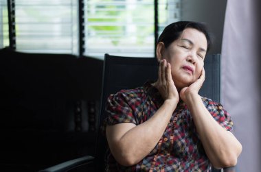 Yaşlı Asyalı kadın evdeki pencerenin yanında oturuyor, son sınıf öğrencisi kederli ve depresif.