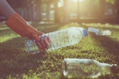 Gönüllü kadın elleri plastik şişeyi yeşil çimlerin üzerinde tutar, bilinçli zihin, geri dönüşüm ve atık yönetimi kavramını ortadan kaldırır