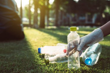 Gönüllü kadın elleri plastik şişeyi yeşil çimlerin üzerinde tutar, bilinçli zihin, geri dönüşüm ve atık yönetimi kavramını ortadan kaldırır