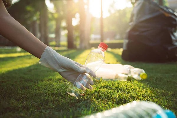 Gönüllü kadın elleri plastik şişeyi yeşil çimlerin üzerinde tutar, bilinçli zihin, geri dönüşüm ve atık yönetimi kavramını ortadan kaldırır