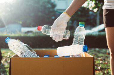 Gönüllü kadın plastik şişeyi halka açık bir parkta karton kutuya koyup geri dönüşüm ve atık yönetimi kavramını yok ediyor.