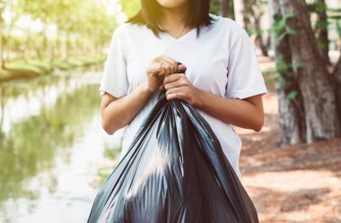 Açık havada siyah renkli çöp torbası taşıyan kadınlar, atık yönetimi ve plastik geri dönüşüm kavramını çöpe atıyor
