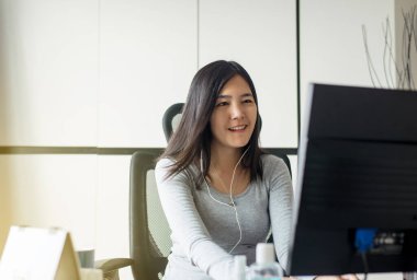 Asyalı kadın evde çalışırken cep telefonu kullanıyor, mutlu ve gülümsüyor, evden çalışıyor.