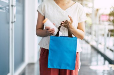 Yeniden kullanılabilir içecek şişesini eko poşetine koyan eller, sağlıklı yeşil, çevre dostu, sıfır atık, bilinçli yaşam tarzı konsepti