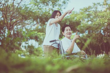 Bakıcı, yaşlı Asyalı kadına iyi bak. Doğada tekerlekli sandalyede oturuyor.