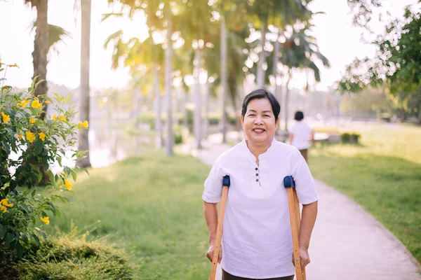 Koltuk değneği kullanan hasta olgun Asyalı kadın dışarıda yürümek için kırık bacakları destekliyor, fizik tedavi kavramı. 