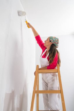 Young girl standing on a ladder painting the walls  clipart