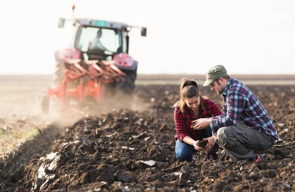 Agricultores examinando sujeira enquanto trator é arar campo — Fotografia de Stock