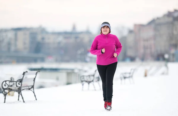 Žena nosí sportovní oblečení a běží na sněhu v zimě — Stock fotografie
